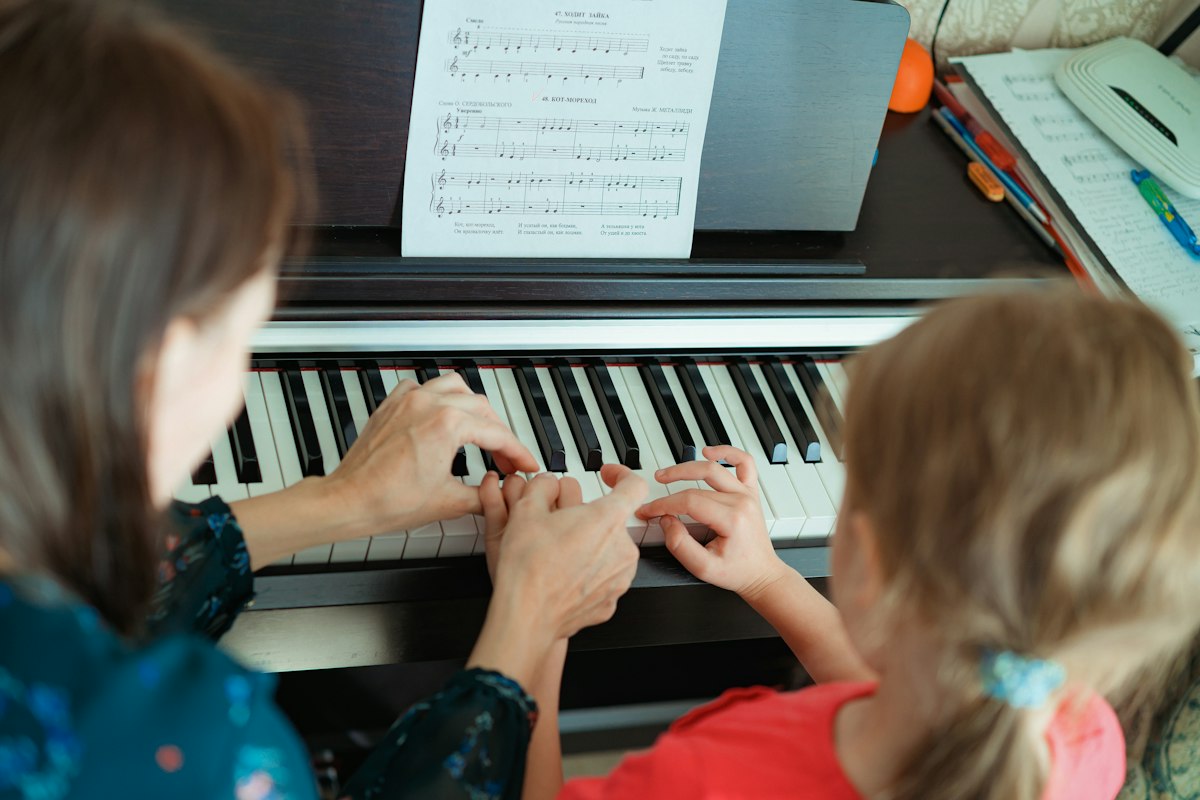 Une professeure de piano guide une élève au clavier