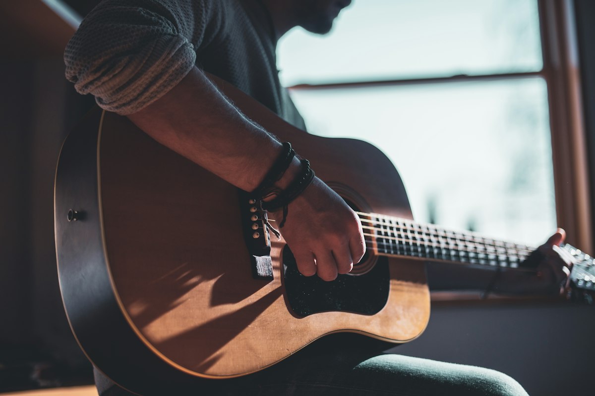 Un guitariste joue de la guitare acoustique près d'une fenêtre